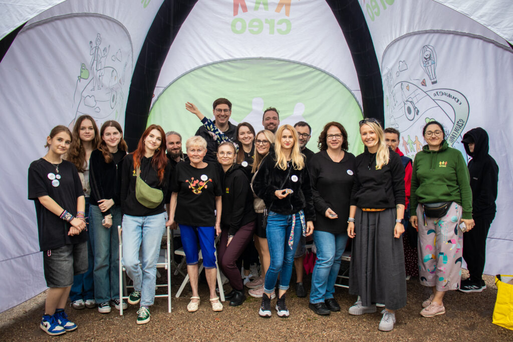 Grupa osób w czarnych bluzach z logo CREO. Pozują do zdjęcia pod dużym dmuchanym namiotem