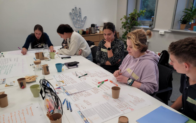 Grupa ludzi siedzi przy stole. Pracują nad projektami.