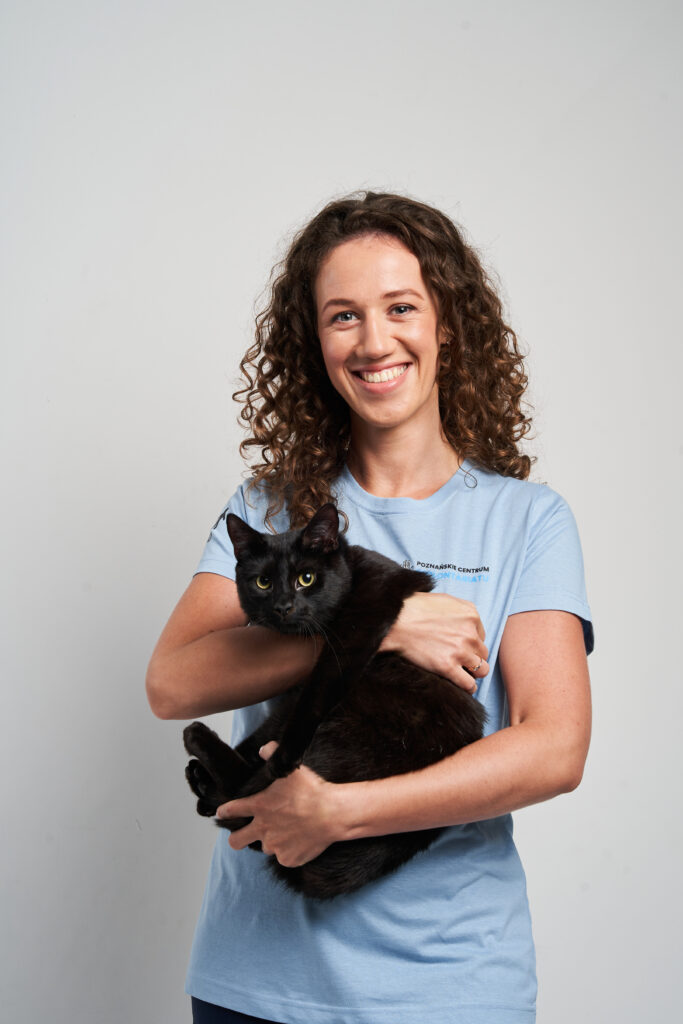 Wolontariuszka w niebieskiej koszulce Poznańskiego Centrum wolontariatu. Trzyma na rękach czarnego kota.