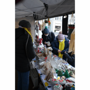 Kiermasz bożonarodzeniowy. Grupka osób stoi przy stoisku.