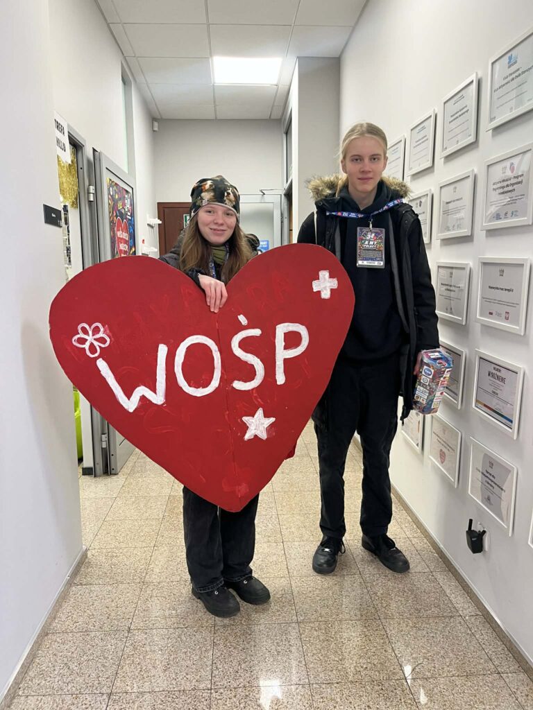 Dwie osoby pozuję w Poznanskim Centrum Wolontariatu. Jedna z nich trzyma wielkie czerwone serce z napisem WOŚP