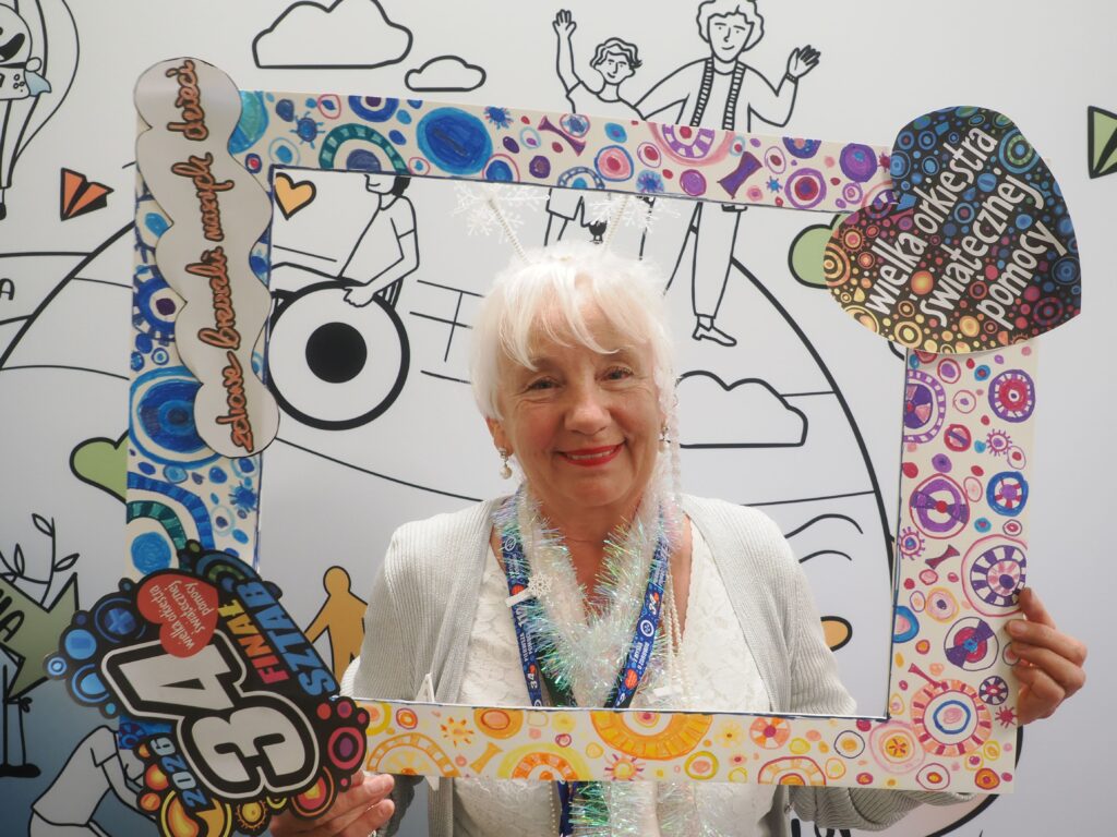 uśmiechnięta seniorka pozuje w ramce do zdjęć. Na ramce napisy 34 finał WOŚP